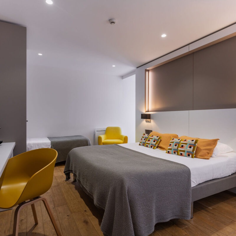 Belle chambre d'hôtel pour 3 personnes à Benodet aux couleurs jaune et taupe. Coussins déco de la marque Vivaraise, grand lit King size et lit individuel. Bureau épuré avec machine à café Nespreso, bouilloire, télévision connectée.