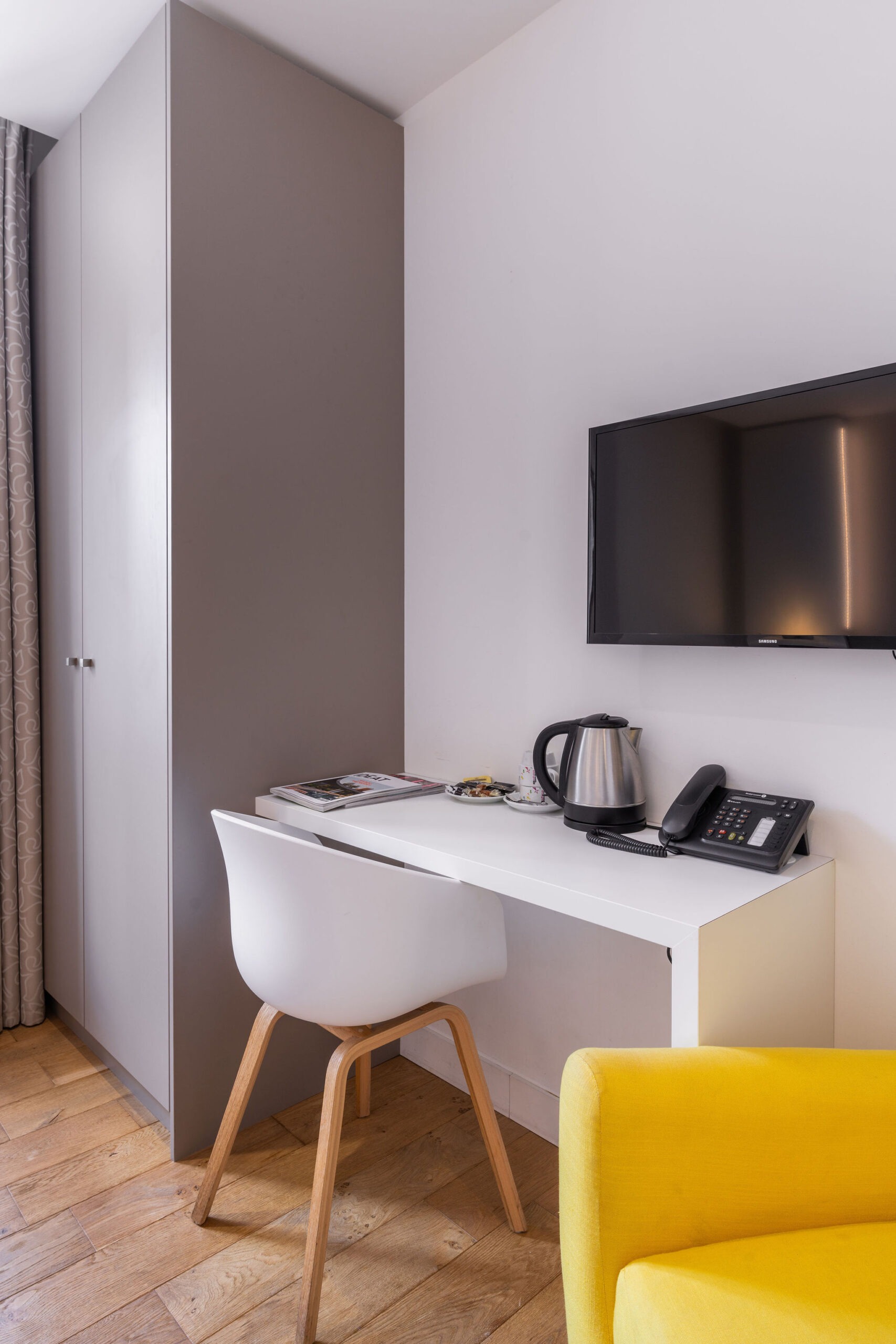 Coin bureau dans une chambre standard de l'hôtel Le Cornouaille, avec une chaise moderne, une bouilloire, un téléphone et une télévision murale.