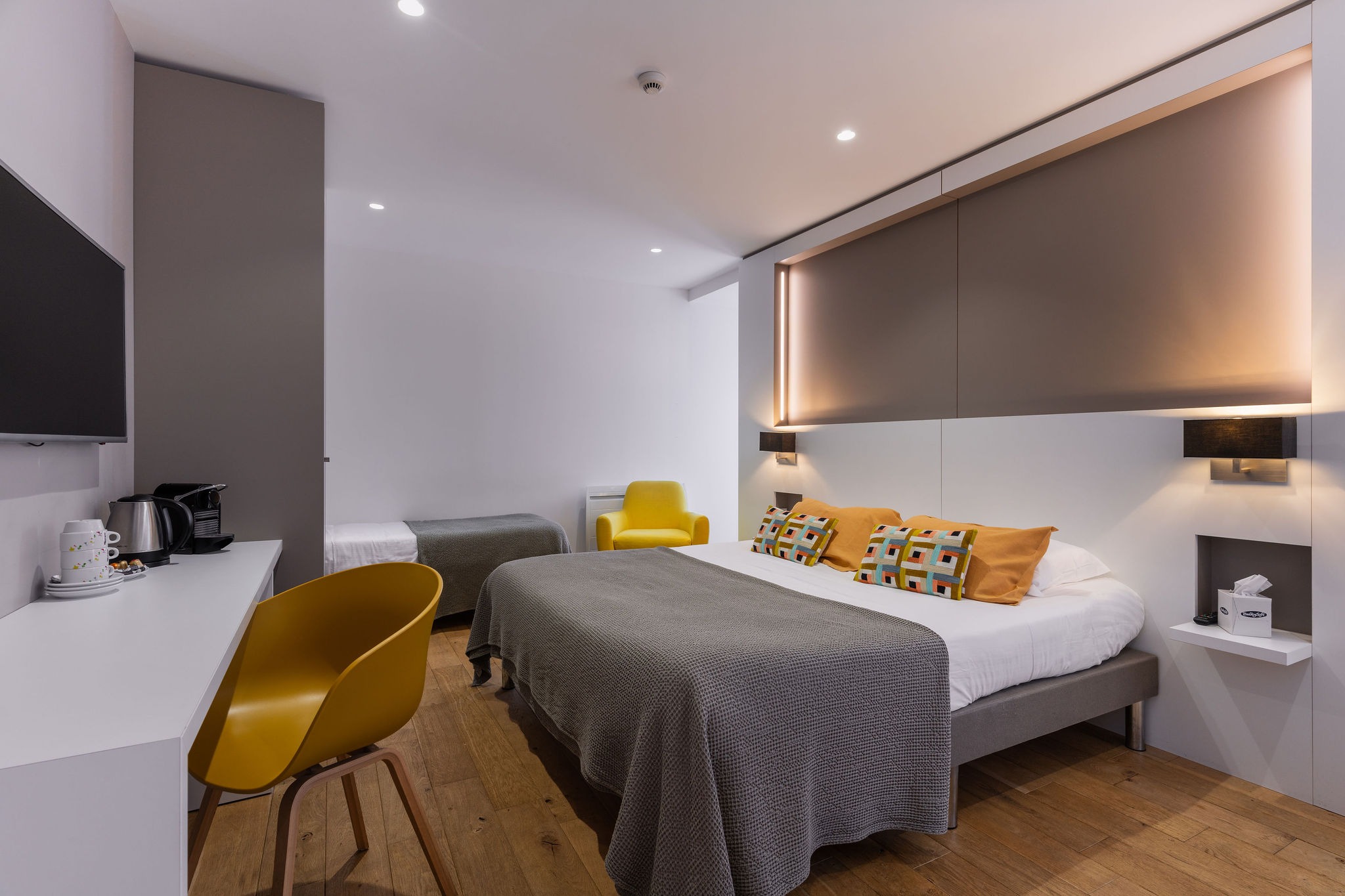 Belle chambre d'hôtel pour 3 personnes à Benodet aux couleurs jaune et taupe. Coussins déco de la marque Vivaraise, grand lit King size et lit individuel. Bureau épuré avec machine à café Nespreso, bouilloire, télévision connectée.