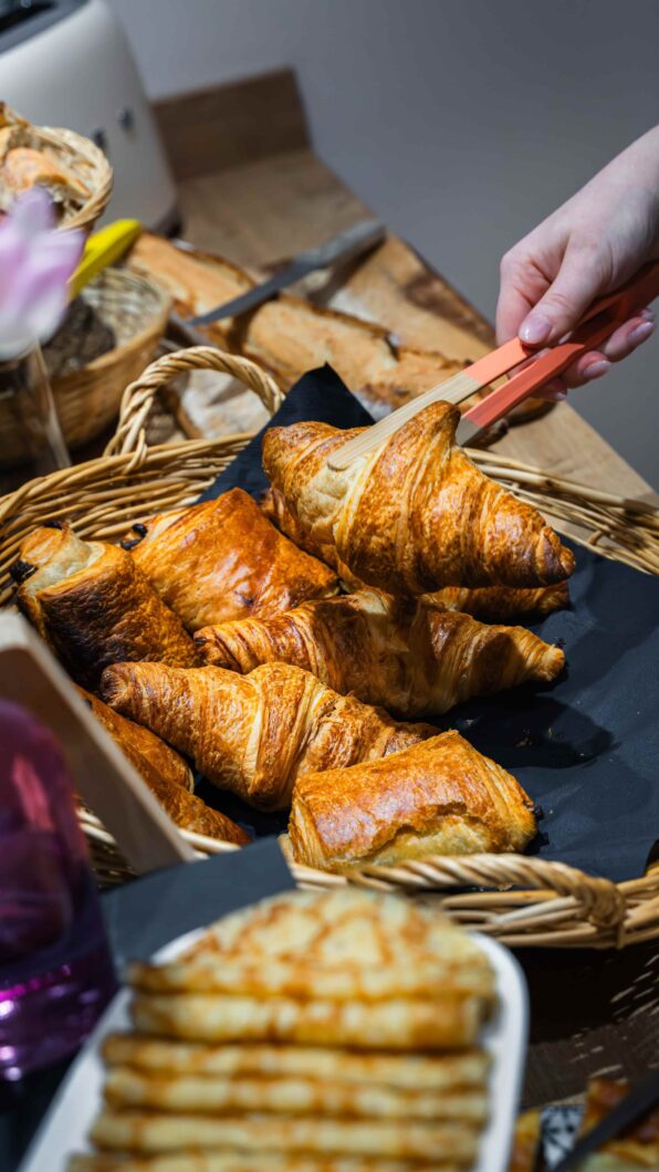 une personne en train de servir un croissant frais sur le buffet. vue d'une partie des produits.